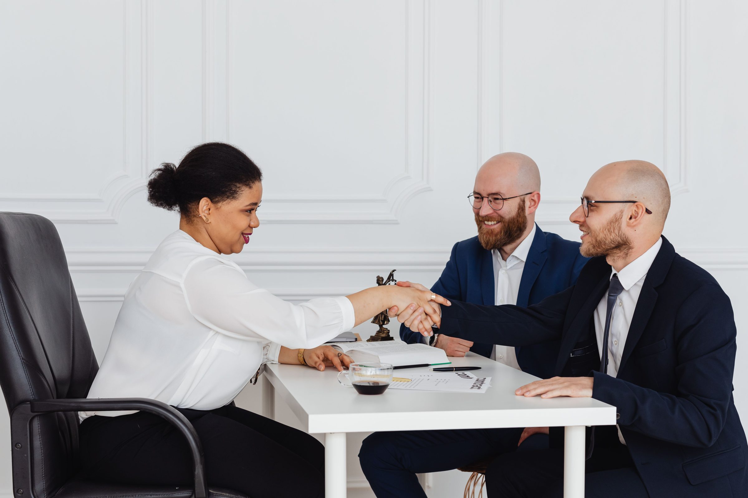 A woman and two men shaking hands across an office table.